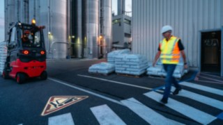 Ein Fußgänger überquert einen Fußgängerüberweg, ein mit dem Linde TruckSpot ausgestatteter Gabelstapler nähert sich. Ein Fußgänger überquert einen Fußgängerüberweg, ein mit dem Linde TruckSpot ausgestatteter Gabelstapler nähert sich.