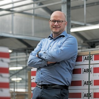 Kai Brendel, Geschäftsführer von ABS Safety, steht vor gestapelten Kartons mit ABS-Logo.